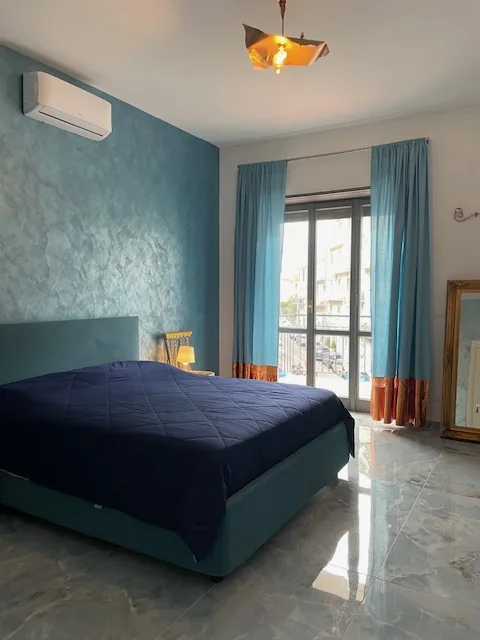 Camera da letto del bilocale Natura con pareti color acqua e tende azzurre